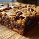 A close-up side view of a thick, chewy chocolate chip cookie bars showing melted chocolate pockets.