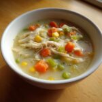 Close-up of a white bowl filled with creamy Chicken Pot Pie Soup featuring shredded chicken, carrots, peas, and corn.