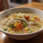 A close-up of a white bowl filled with creamy Chicken Pot Pie Soup featuring shredded chicken, carrots, peas, and corn.