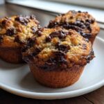 Three freshly baked Chocolate Chip Banana Muffins with melted chocolate chips on a white plate.