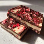 Two stacked pieces of Chocolate Covered Strawberry Bark showing layers of dark chocolate, white filling, and red freeze-dried strawberry pieces.