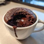 Close-up of a freshly baked Chocolate Lava Mug Cake in a white mug, showing the molten chocolate center oozing out.