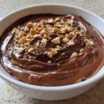 A close-up of rich Chocolate Peanut Butter Cheesecake Dip topped with chopped peanuts in a white bowl.