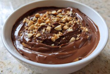 A close-up of rich Chocolate Peanut Butter Cheesecake Dip topped with chopped peanuts in a white bowl.