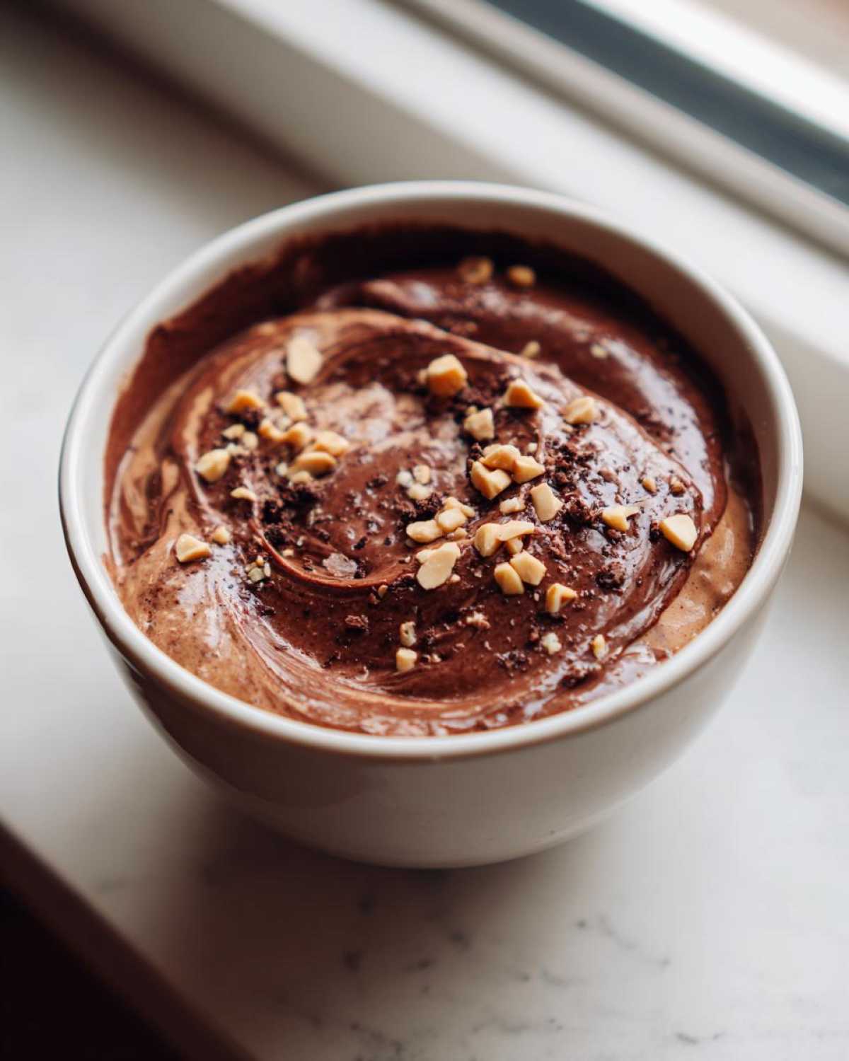 Close-up of rich Chocolate Peanut Butter Cheesecake Dip swirled in a white bowl, topped with chopped peanuts.