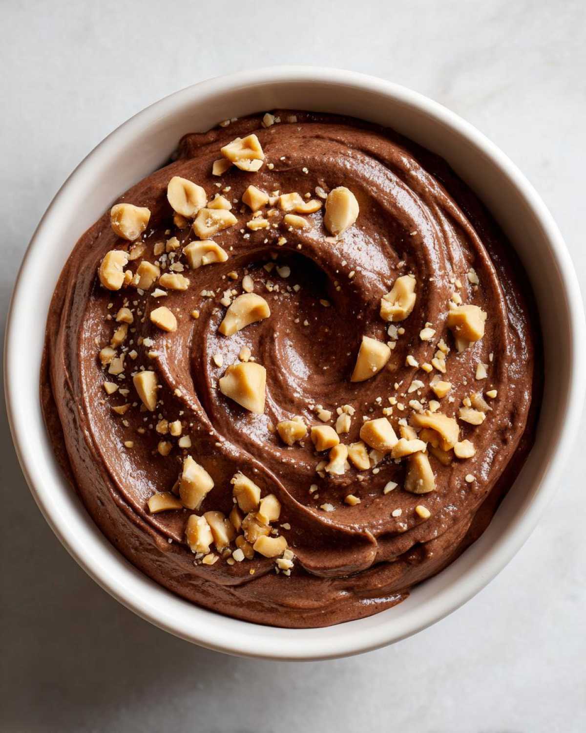 Overhead view of rich Chocolate Peanut Butter Cheesecake Dip swirled in a white bowl and topped with chopped peanuts.