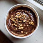 Overhead view of Chocolate Peanut Butter Cheesecake Dip topped with melted chocolate swirls and chopped peanuts in a white bowl.