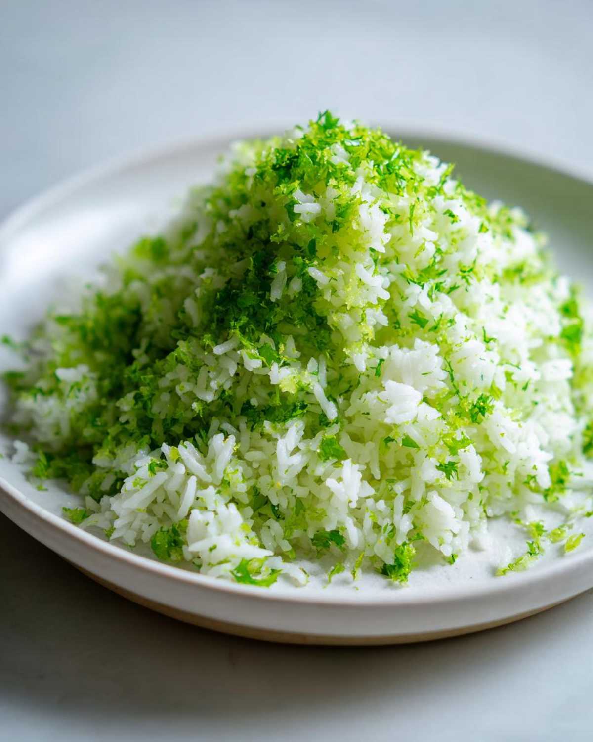 A mound of fluffy Cilantro Lime Rice topped generously with bright green lime zest and chopped cilantro.