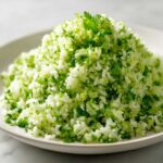 A close-up of a fluffy mound of bright green Cilantro Lime Rice garnished with fresh cilantro leaves.