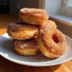 A stack of freshly made Cinnamon Sugar Air Fryer Donuts coated heavily in sparkling cinnamon sugar, resting on a white plate.