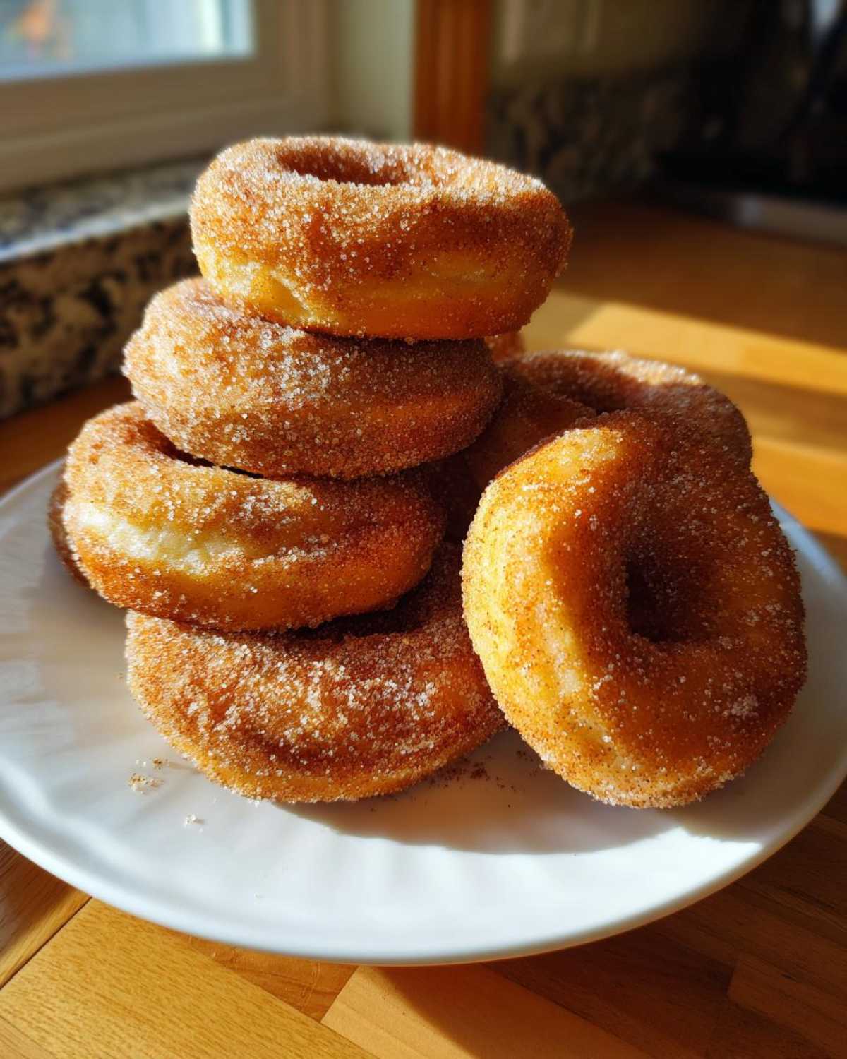 A stack of golden brown Cinnamon Sugar Air Fryer Donuts generously coated in sparkling cinnamon sugar, resting on a white plate.