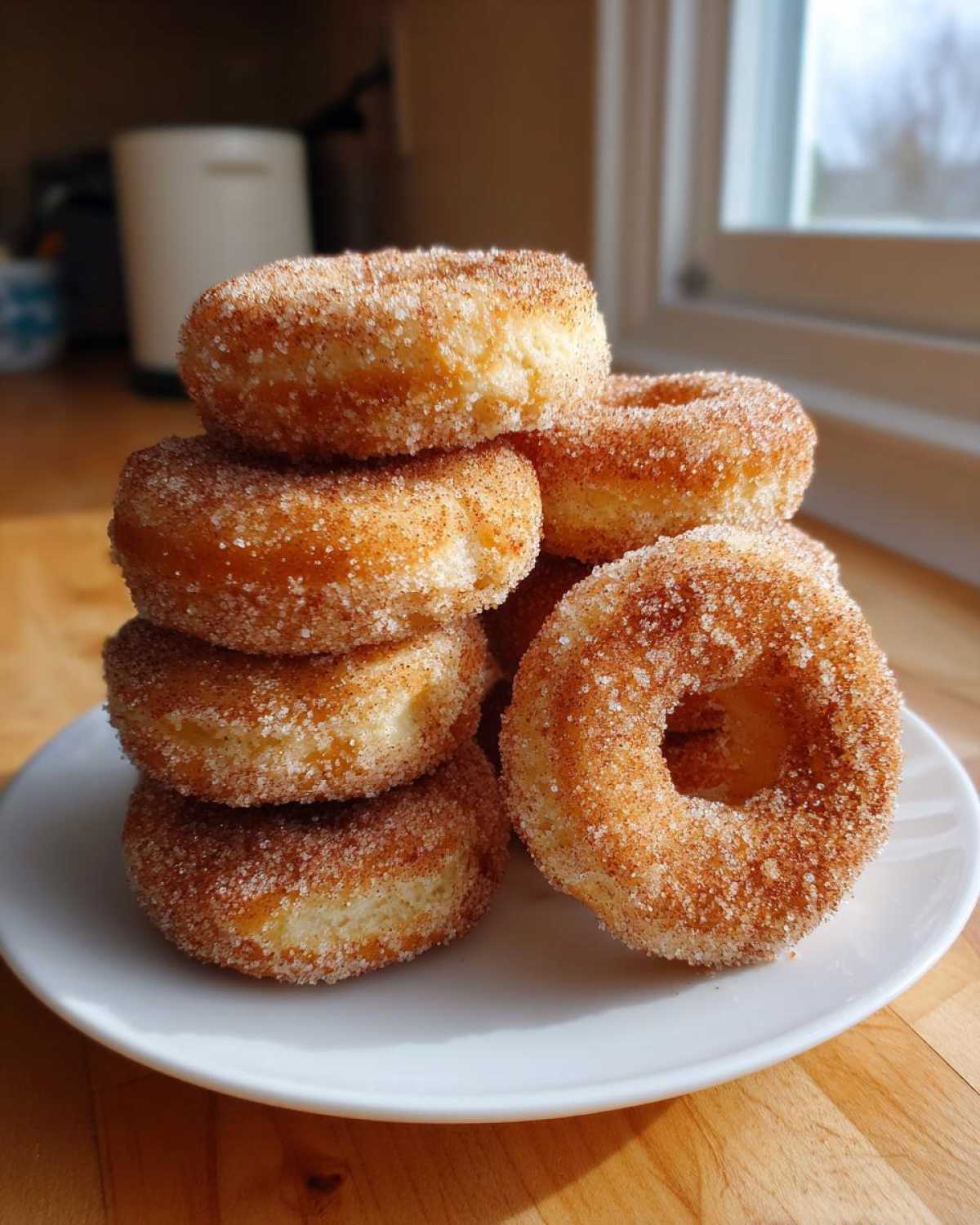 A stack of freshly made Cinnamon Sugar Air Fryer Donuts heavily coated in cinnamon sugar, resting on a white plate.