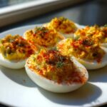 Five halves of Classic Deviled Eggs with Dill Pickle Relish, topped with paprika and fresh dill, served on a white plate.