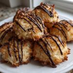 A pile of golden brown Coconut Macaroons with Dark Chocolate Drizzle stacked on a white plate.