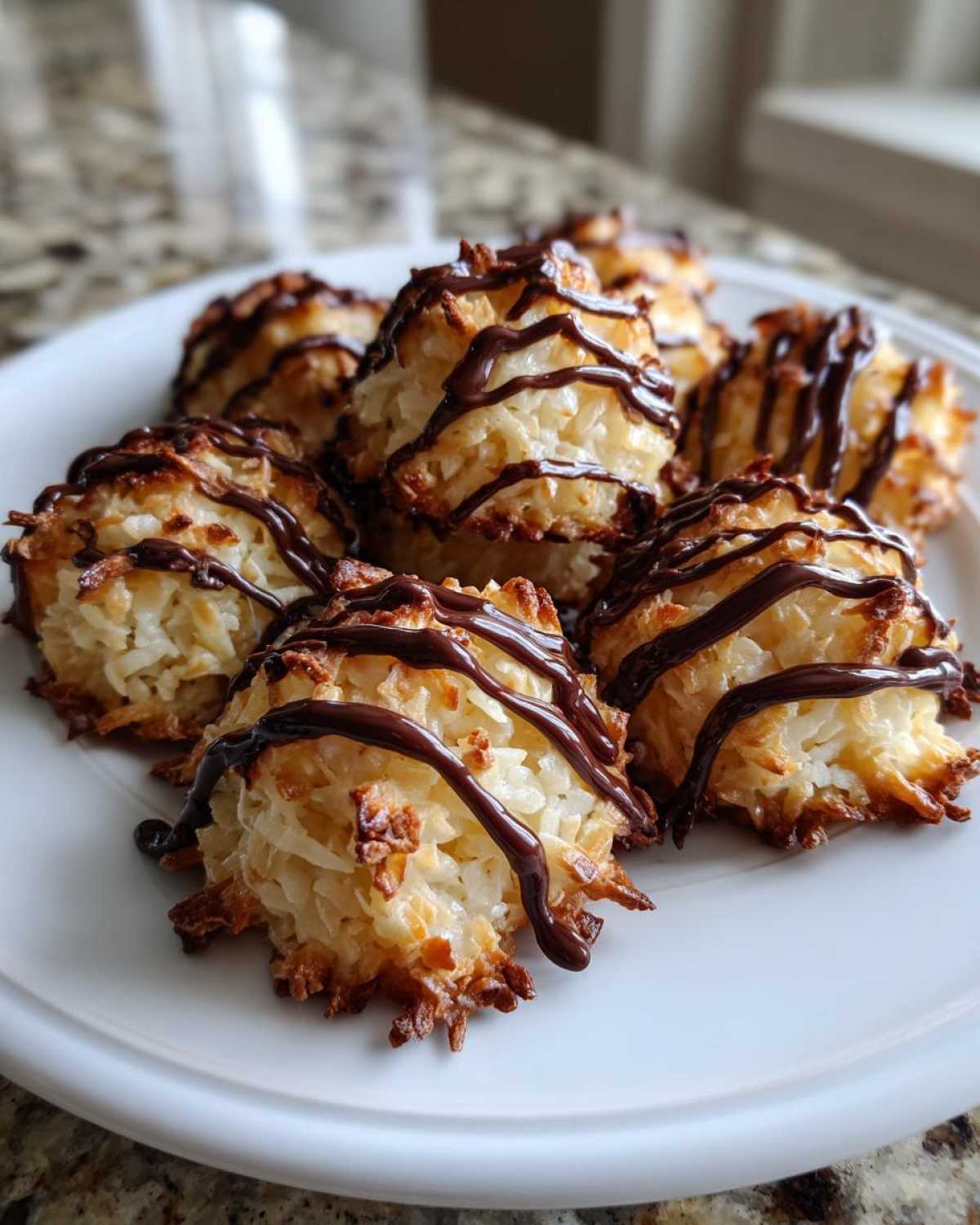 Close-up of baked Coconut Macaroons with Dark Chocolate Drizzle arranged on a white plate.