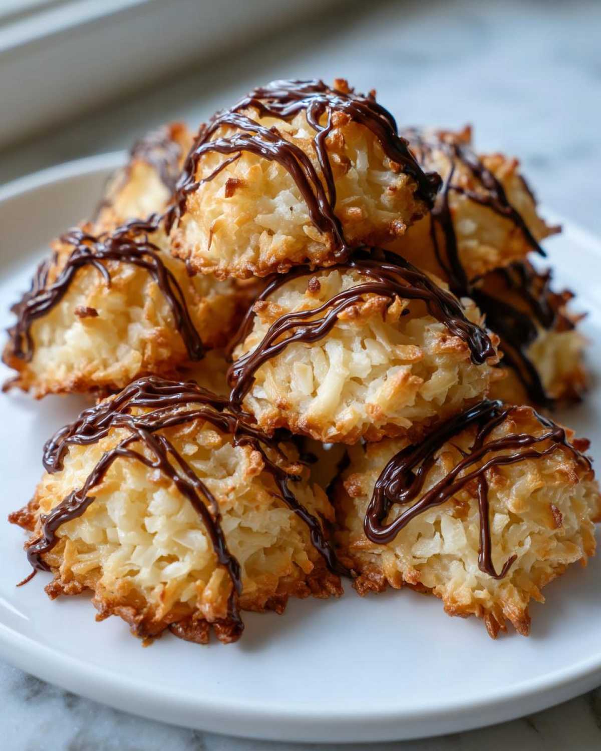 A stack of golden-brown Coconut Macaroons with Dark Chocolate Drizzle on a white plate.
