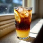 A tall glass of layered Cold Brew Lemonade, showing dark coffee over bright yellow lemonade, filled with ice and garnished with a lemon slice.