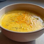 Close-up of a bowl filled with creamy, yellow Copycat Broccoli Cheddar Soup topped with melted cheddar.