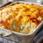 A close-up of baked Copycat Cracker Barrel Hashbrown Casserole topped with melted, bubbly cheddar cheese.