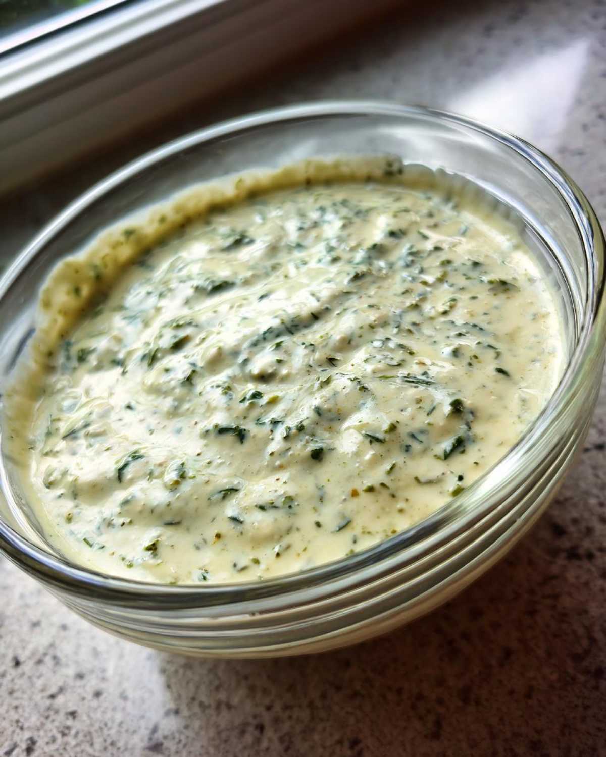 Close-up of creamy Copycat Olive Garden Salad Dressing with visible green herbs in a clear glass bowl.