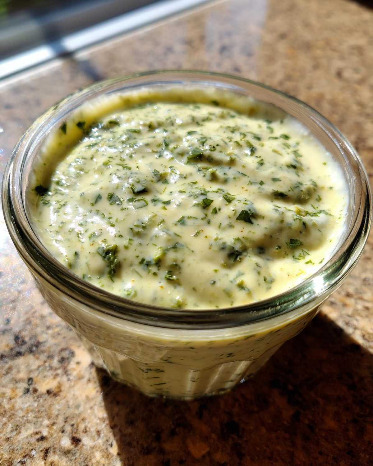 Close-up of creamy Copycat Olive Garden Salad Dressing speckled with green herbs in a glass jar.