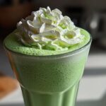 Close-up of a vibrant green Copycat Shamrock Shake topped with fluffy mint whipped cream.