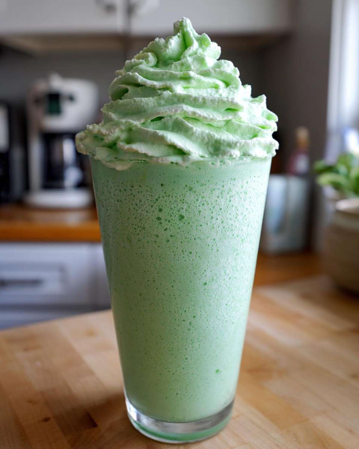 A tall glass filled with a vibrant green Copycat Shamrock Shake topped high with mint whipped cream.