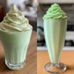 Two glasses of bright green Copycat Shamrock Shake topped with generous swirls of mint whipped cream.