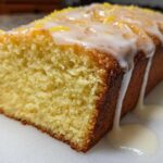 A moist slice of Copycat Starbucks Iced Lemon Loaf with thick white glaze dripping down the side and lemon zest on top.