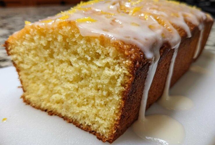 A moist slice of Copycat Starbucks Iced Lemon Loaf with thick white glaze dripping down the side and lemon zest on top.