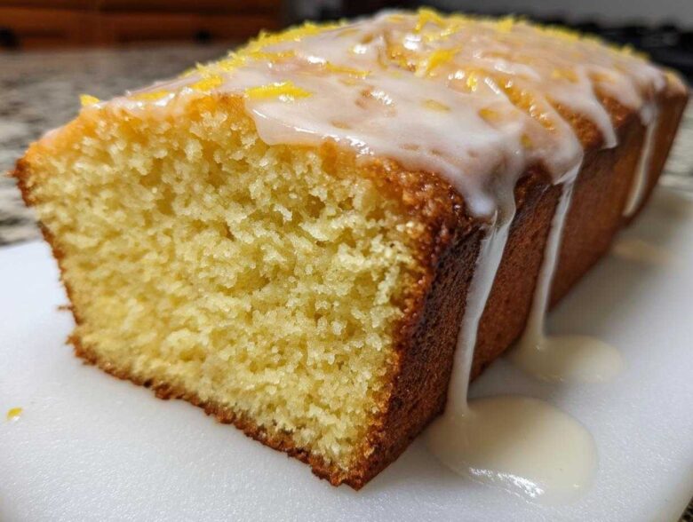 A moist slice of Copycat Starbucks Iced Lemon Loaf with thick white glaze dripping down the side and lemon zest on top.