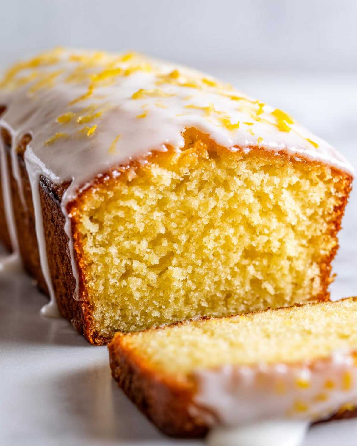 A close-up of a sliced Copycat Starbucks Iced Lemon Loaf with thick white glaze and lemon zest topping.