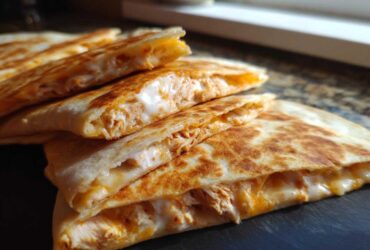 Close-up of stacked, grilled chicken quesadilla wedges oozing with melted cheese and Copycat Taco Bell Chicken Quesadilla Sauce.
