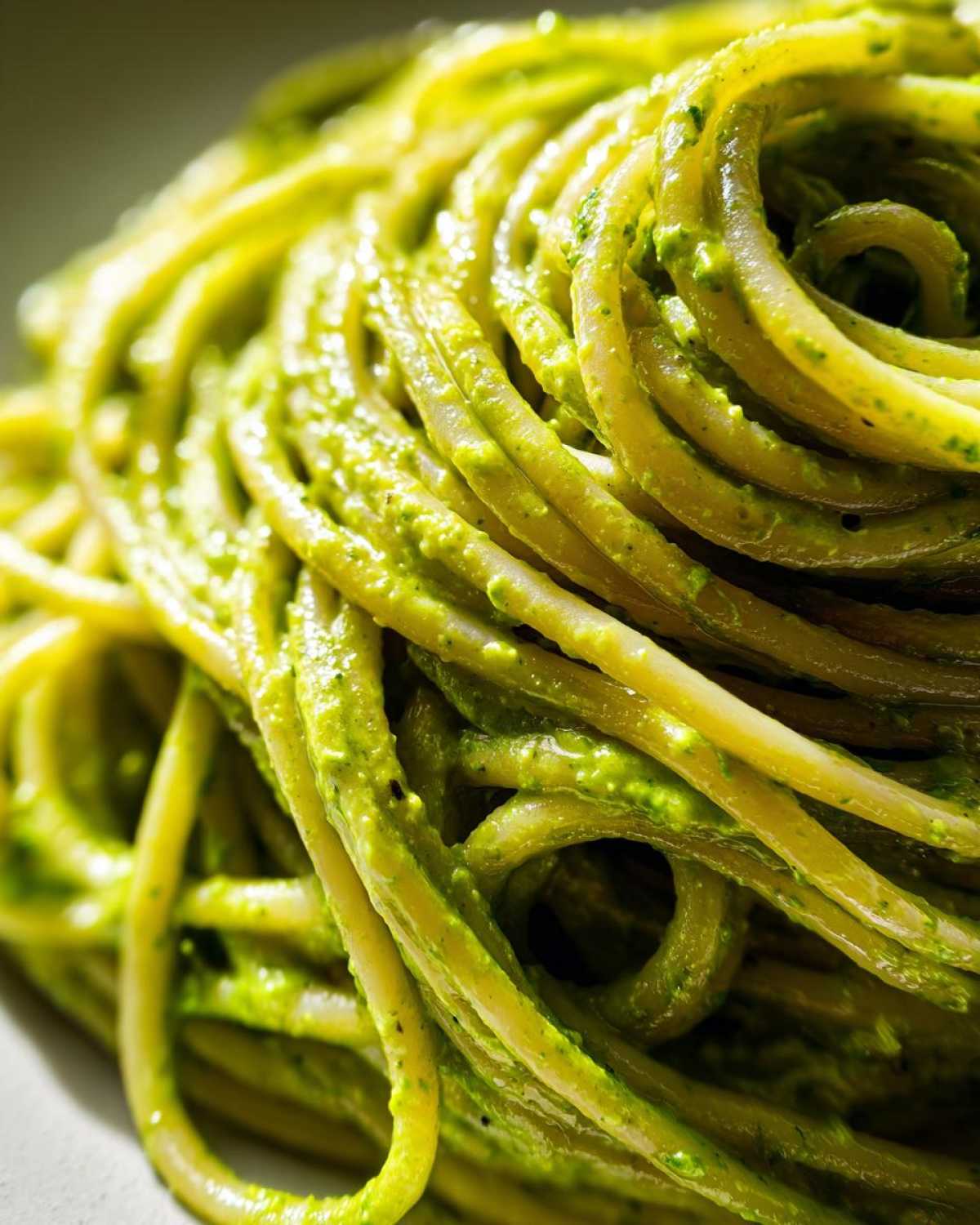 Extreme close-up of spaghetti noodles coated in vibrant green Creamy Avocado Pasta sauce.