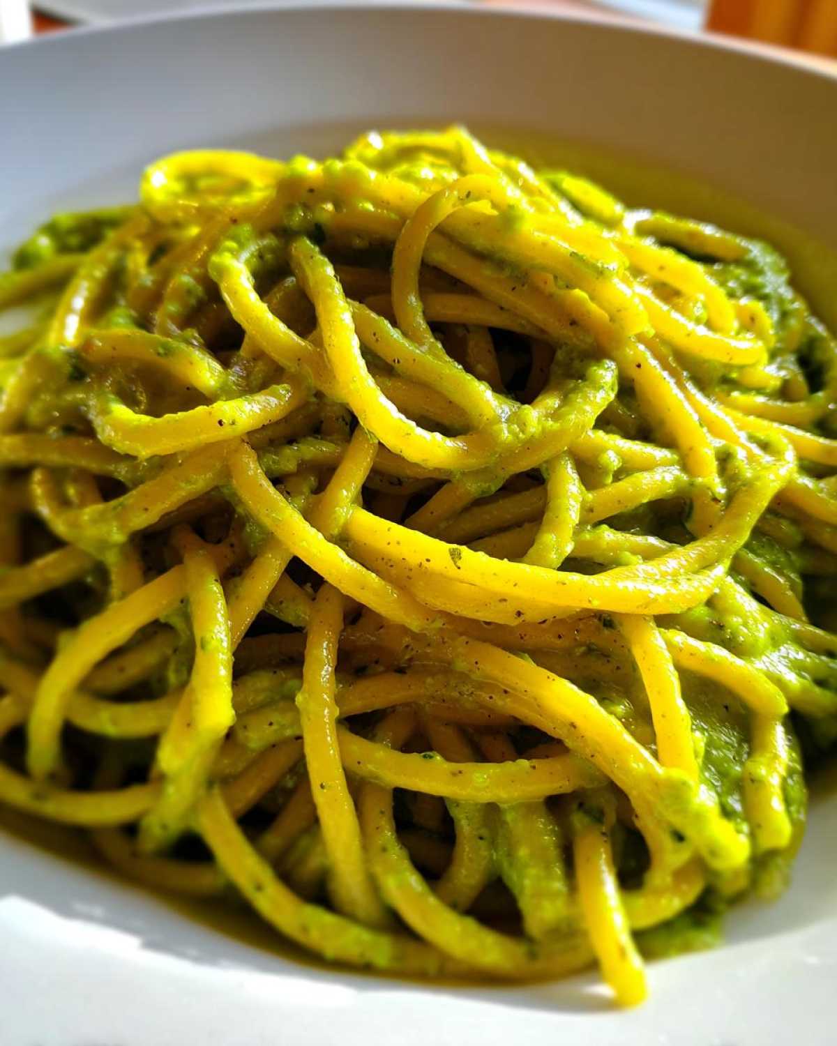 Close-up of thick spaghetti coated in vibrant green Creamy Avocado Pasta sauce served in a white bowl.