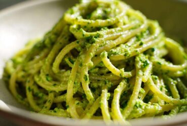 A close-up, vibrant shot of spaghetti coated thickly in bright green Creamy Avocado Pasta sauce.