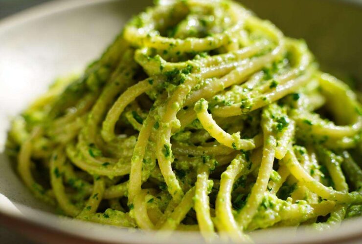 A close-up, vibrant shot of spaghetti coated thickly in bright green Creamy Avocado Pasta sauce.