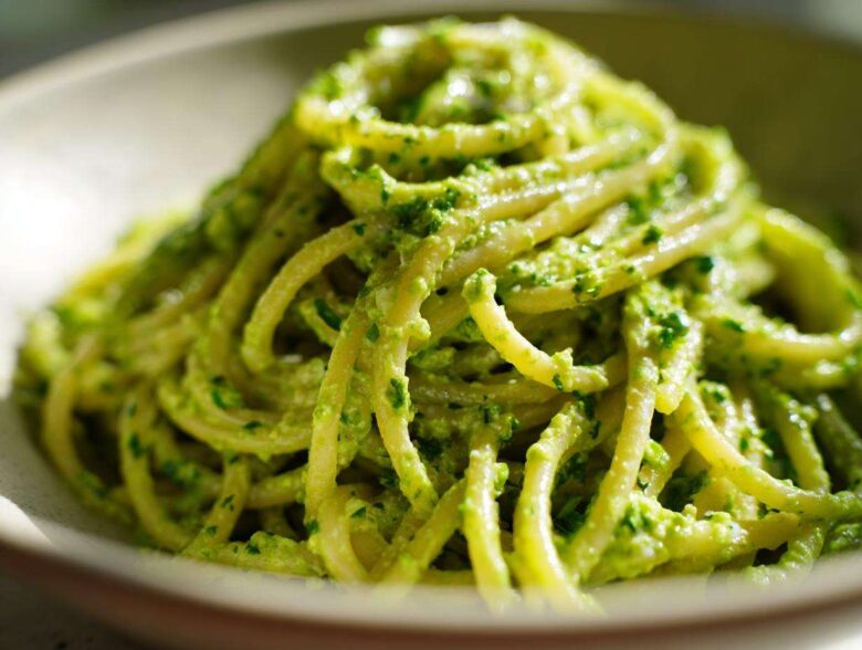 A close-up, vibrant shot of spaghetti coated thickly in bright green Creamy Avocado Pasta sauce.