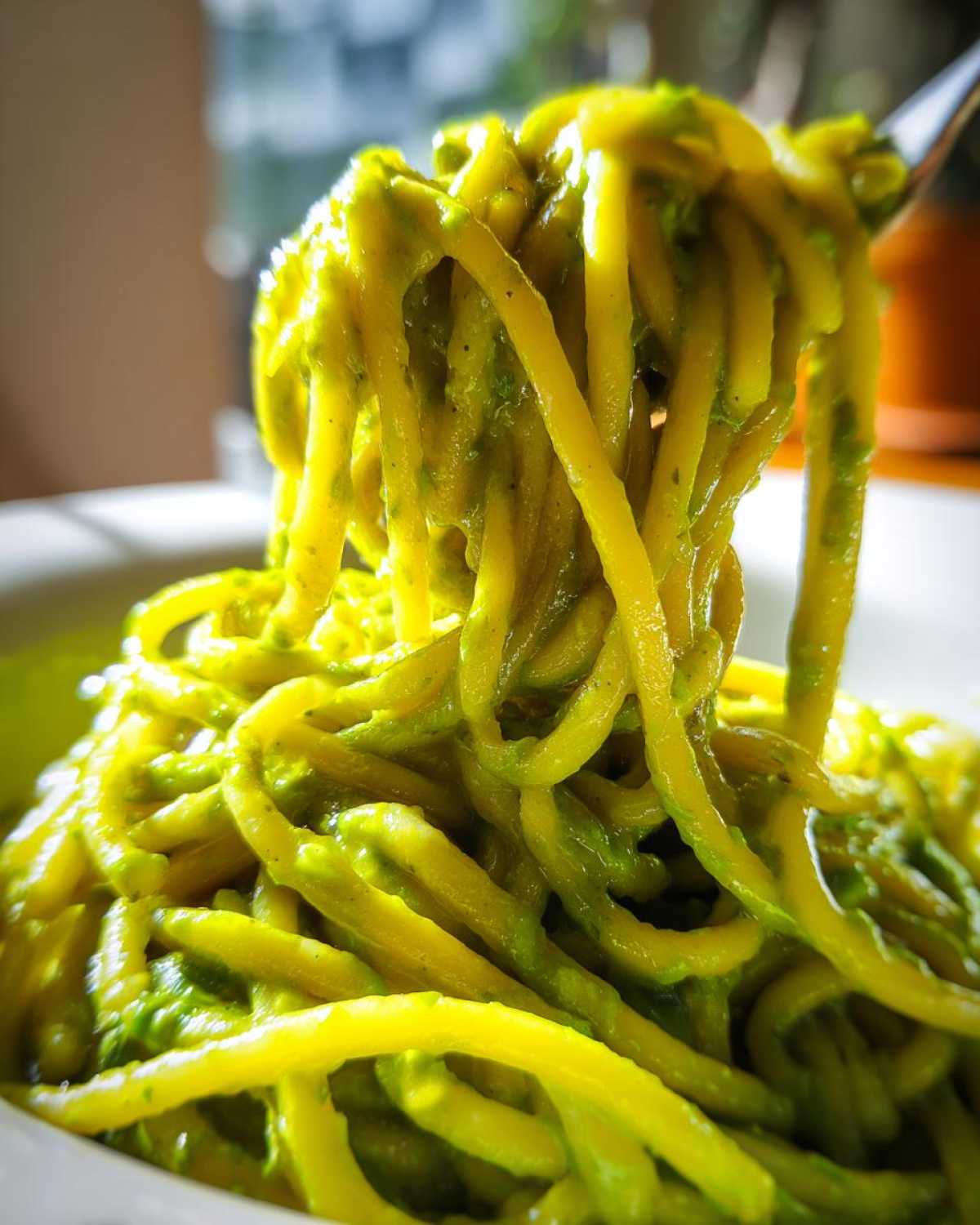 A close-up shot of thick pasta noodles coated in bright green Creamy Avocado Pasta sauce being lifted by a fork.