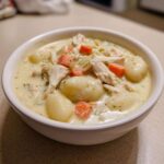 A close-up of a white bowl filled with rich Creamy Chicken Gnocchi Soup, featuring shredded chicken, soft gnocchi, and diced carrots.