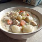 A close-up of a white bowl filled with rich Creamy Chicken Gnocchi Soup, featuring plump gnocchi, chicken pieces, carrots, and celery.