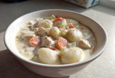 A close-up of a white bowl filled with rich Creamy Chicken Gnocchi Soup, featuring plump gnocchi, chicken pieces, carrots, and celery.