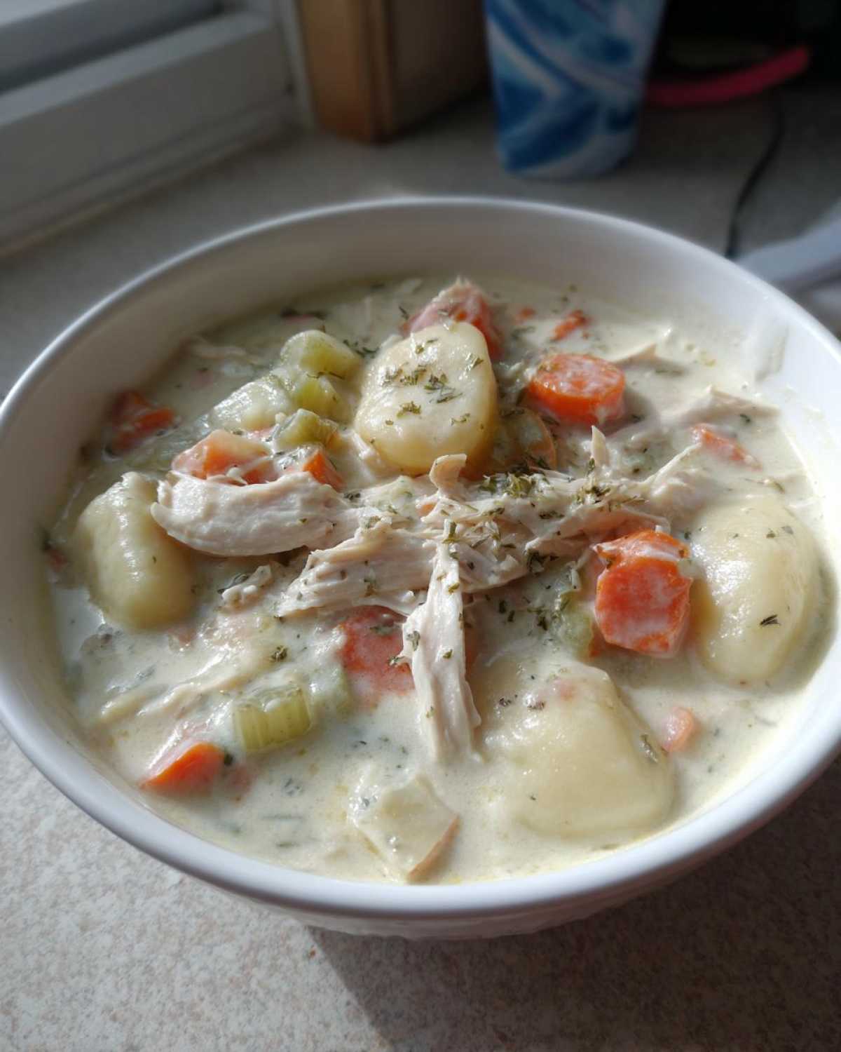Close-up of a white bowl filled with rich Creamy Chicken Gnocchi Soup, featuring shredded chicken, soft gnocchi, carrots, and celery.