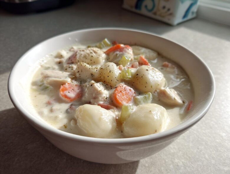 A close-up of a white bowl filled with rich Creamy Chicken Gnocchi Soup, featuring plump gnocchi, chicken pieces, carrots, and celery.