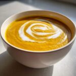 Close-up of a vibrant orange Creamy Coconut Lentil Soup topped with a white coconut cream swirl.