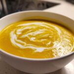 Close-up of vibrant orange Creamy Coconut Lentil Soup swirled with white coconut cream in a white bowl.
