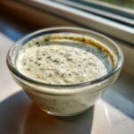 Close-up of creamy Copycat Olive Garden Salad Dressing topped with dried herbs in a small glass bowl.