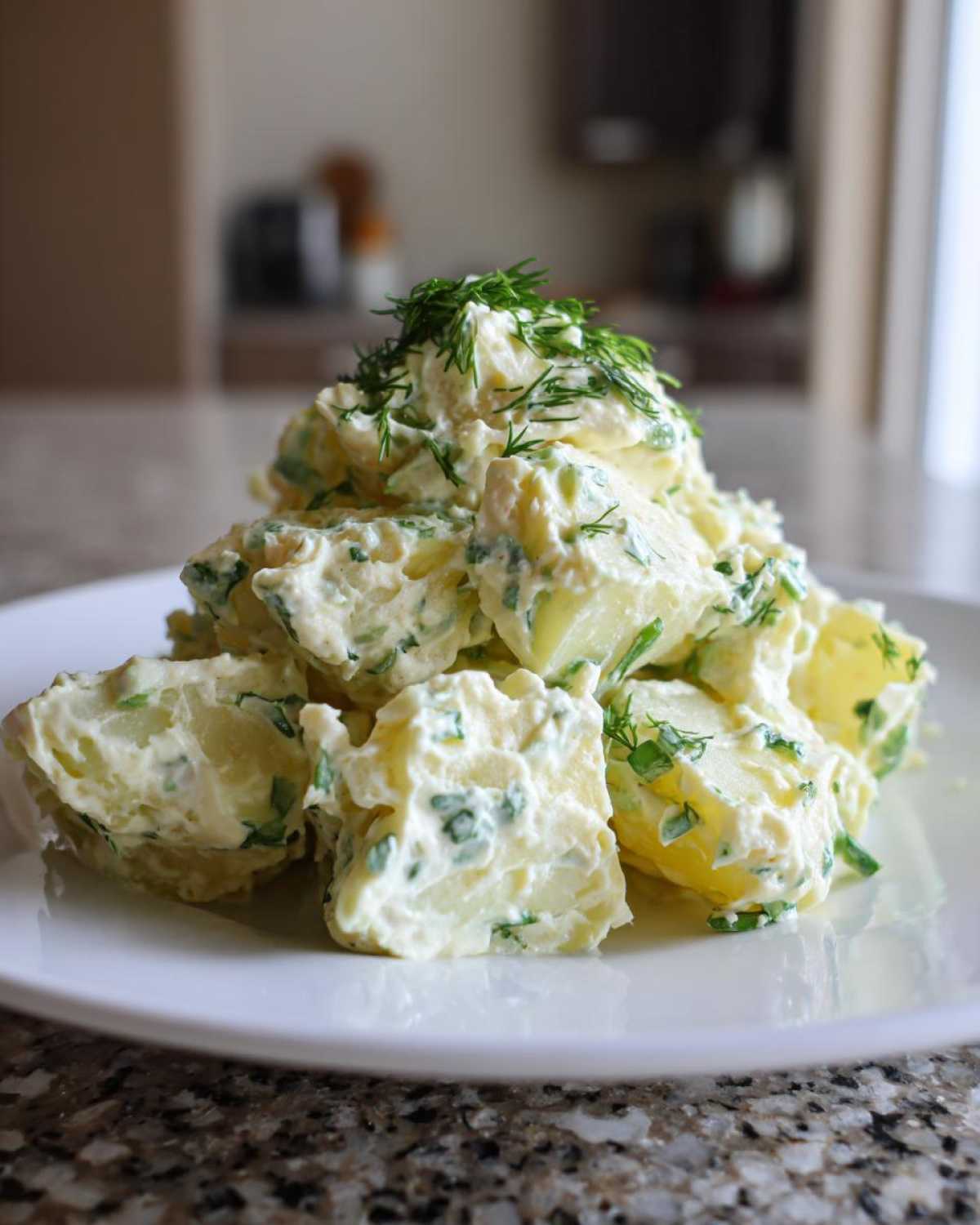 A mound of Creamy Dill Potato Salad made with chunks of potato coated in a light dressing and topped with fresh dill.