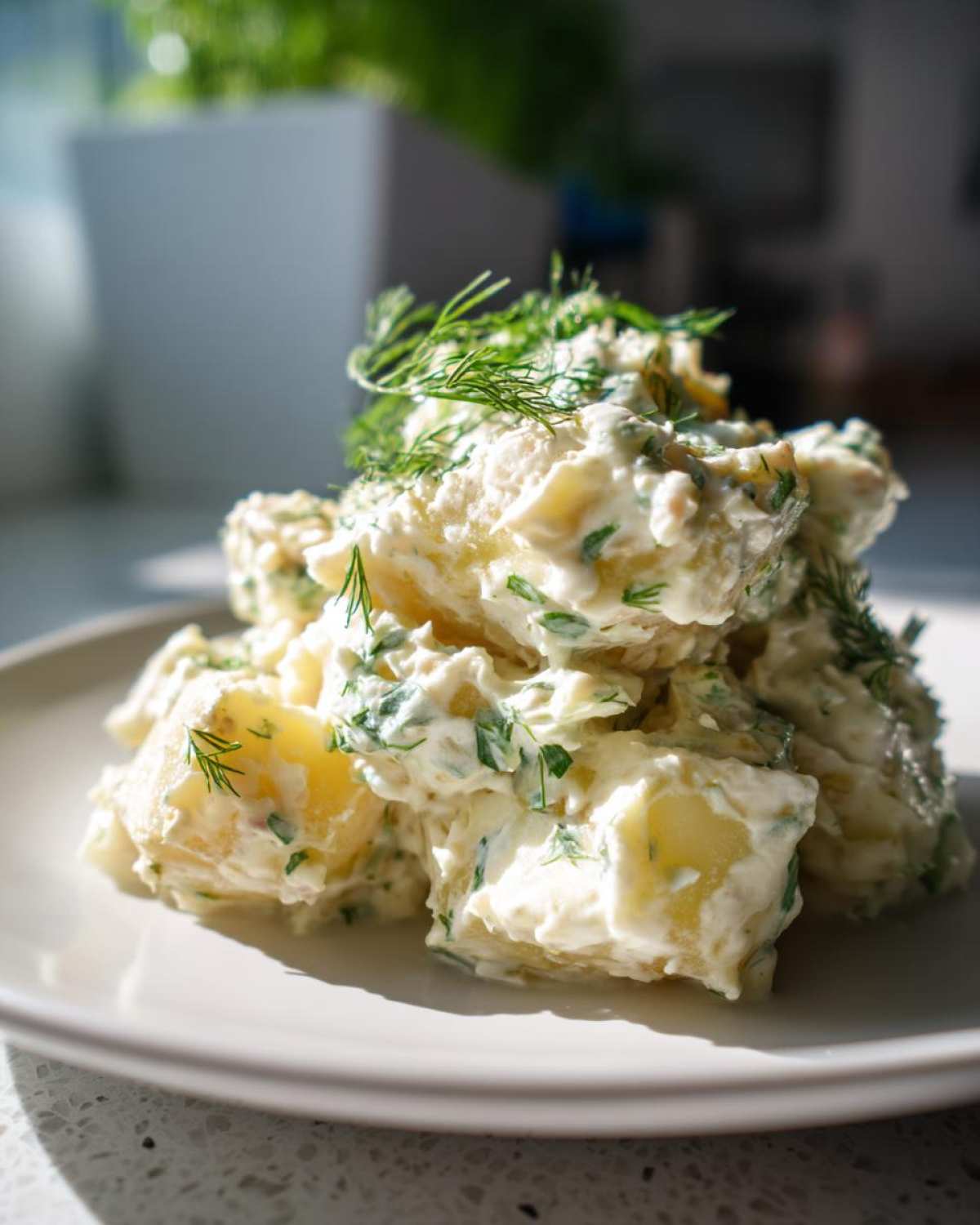A close-up of a mound of Creamy Dill Potato Salad, featuring chunks of potato coated in a white dressing and topped with fresh dill.