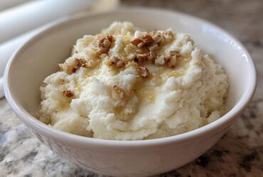 A white bowl filled with fluffy Creamy Garlic Mashed Cauliflower, topped with chopped nuts and a drizzle of liquid.